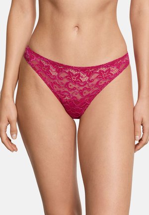 Kobieta w różowym koronkowym bikini w kwiatowy wzór na jasnym tle, pokazująca tors i górną część ud.