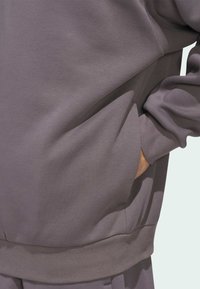 Sivi dukserica napravljena od mekog materijala, sa rebrastim donjim rubom i manžetama, sa integriranim bočnim džepom u dizajnu.