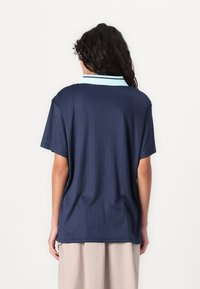 Marinblå polo t-shirt med ljusblå krage, korta ärmar och vertikal randig textur, utformad för en avslappnad passform.