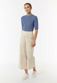 Blue knit top with short sleeves, paired with beige wide-leg trousers and white sneakers; smooth texture, horizontal stripe pattern.