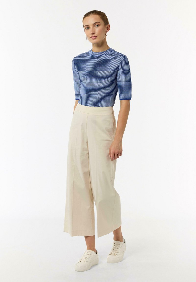 Blue knit top with short sleeves, paired with beige wide-leg trousers and white sneakers; smooth texture, horizontal stripe pattern.