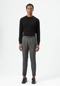 Schwarzes Langarmhemd kombiniert mit grauer, plissierter Hose mit Gürtel. Die Schuhe sind schwarz, mit rundem Design und ohne sichtbare Muster.