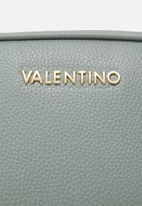 Pelle grigia testurizzata con una finitura leggermente granulosa, caratterizzata dal nome del marchio "VALENTINO" impresso in lettere metalliche dorate.