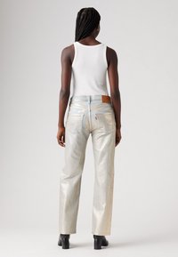 Jeans in denim argentato lucido con vestibilità rilassata, dotati di un'etichetta in pelle alla vita, tasche posteriori a toppa e una leggera texture lucida.