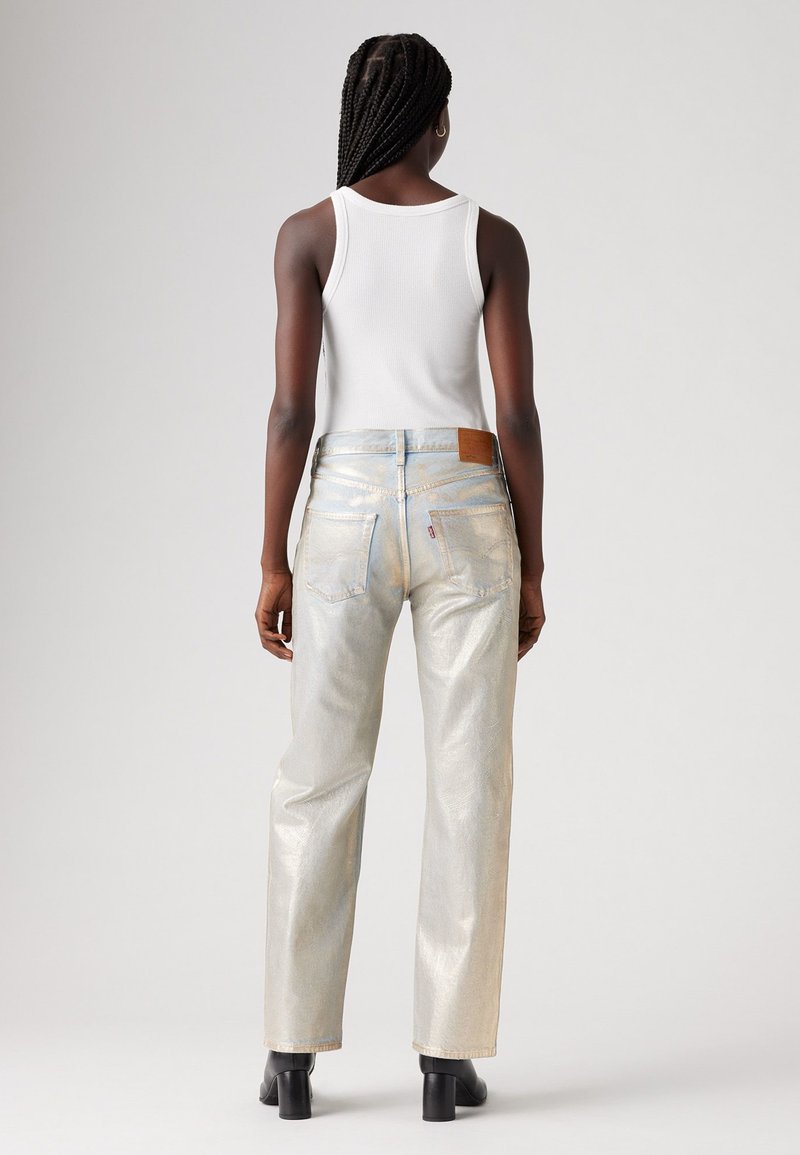 Jean en denim argenté brillant avec une coupe décontractée, présent avec une patch en cuir au niveau de la taille, des poches arrière en patch et une texture légèrement brillante.