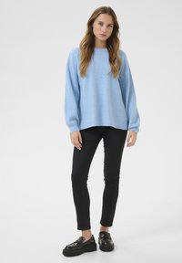 Světle modrý oversize svetr s dlouhými rukávy, kulatým výstřihem a měkkou texturou. Černé skinny džíny a robustní černé mokasíny doplňují outfit.