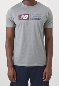 Szara koszulka z krótkim rękawem z czerwono-granatowym wzorem logo "New Balance" na przodzie. Wykonana z miękkiego, gładkiego materiału.