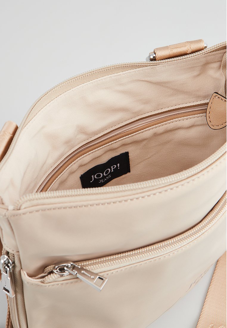 Beige Handtasche mit einer strukturierten, glatten Außenseite, doppelt zipbaren Fächern und einem markierten Innenlabel. Mit abnehmbarem Tragegurt.