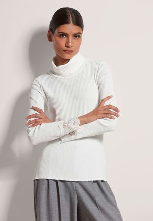Witte geribde turtleneck met lange mouwen en kanten accenten bij de manchetten. De zoom is licht golvend, wat zorgt voor een textuur effect.