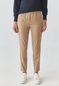 Beige, op maat gemaakte broek met een elastische tailleband, taps toelopende pijpen en zijnaad. Gecombineerd met witte sneakers.