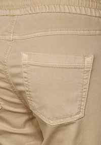 Beiga bomullsbyxor med en jämn textur, elastisk midja och en enda bakficka med förstärkt sömnad.