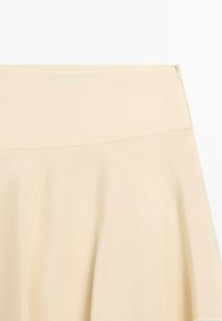 Crèmekleurige rok met hoge taille, een gladde brede tailleband en zachte plooien, afgebeeld op een effen witte achtergrond.