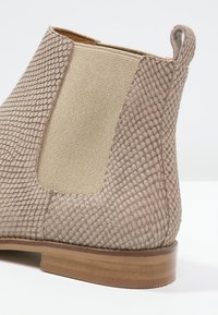 Beżowe botki za kostkę z teksturowanego materiału w wzór reptila oraz gładkimi panelami z tkaniny. Drewniany obcas z solidną podstawą i zaokrąglonym noskiem.