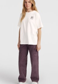 Off-white katoenen T-shirt met korte mouwen en een borstprint. Gecombineerd met loszittende paarse corduroy broek en witte sneakers.