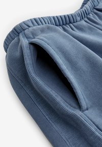 Shorts en coton bleu avec une taille côtelée et des poches latérales, présentant une texture douce et une coupe décontractée, avec des coutures détaillées visibles.
