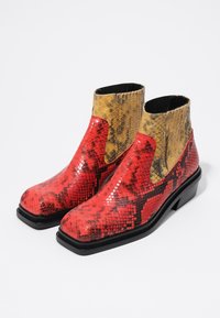 Stivali alla caviglia con motivo a serpente rosso e giallo, dalla finitura liscia e lucida, con suole nere e pannelli laterali elasticizzati.