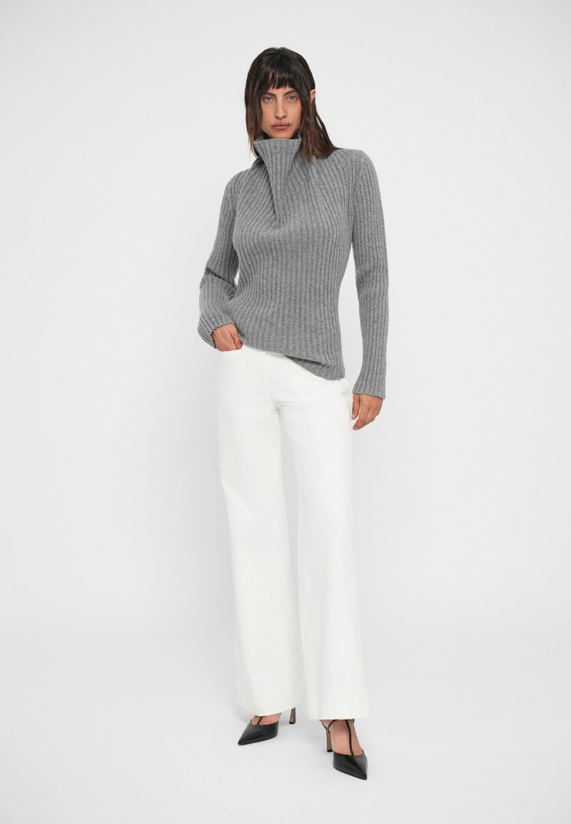 Gray ribbed sweater with a high collar, paired with white wide-leg pants and black pointed-toe heels. Plain white background.