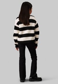 Schwarz-weiß gestreifter Pullover mit gerippter Textur, langen Ärmeln und lockerer Passform. Kombiniert mit dunklen Jeans und schwarzen Schuhen.