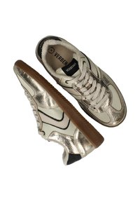 Metallische gouden en crèmekleurige sneakers met een gestructureerde afwerking, vetersluiting, zwarte accenten en een bruine rubberen zool. "VERBENAS" branding zichtbaar.