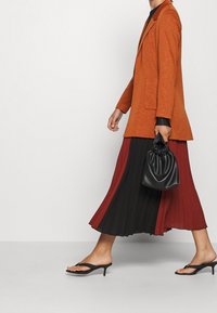 Rust-colored blazer, black and burgundy pleated skirt, black mini bag, and black heeled sandals; smooth textures and layered design elements.