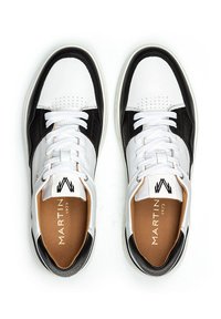 Zapatillas blancas y negras con parte superior de cuero liso, puntera redondeada, detalles perforados, cordones blancos y plantilla color marrón con logo.