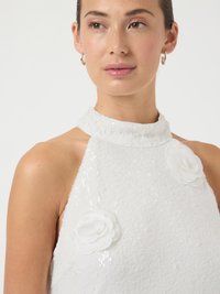 Λευκή αμάνικη μπλούζα με παγιέτες και υφή, με δύο λευκά υφασμάτινα λουλούδια στο στήθος και ψηλό λαιμό.