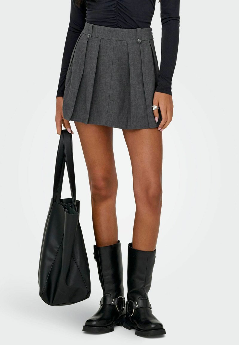 Mini-jupe plissée grise avec deux boutons sur le devant, assortie à un sac fourre-tout noir et des bottes noires montantes. Texture lisse et coupe cintrée.