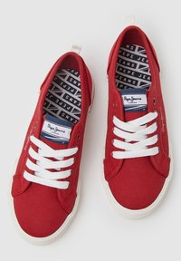 Rote Leinwand-Sneaker mit weißen Schnürsenkeln und Gummisohlen. Innenausstattung mit einer blau-weißen, gebrandeten Einlegesohle. Einfaches, flaches Design.