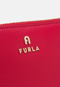Rdeča usnjena torbica z zadrgo, ki prikazuje embosirano "Furla" logo v zlati barvi, z teksturirano površino in zlatimi podrobnostmi zadrge. Kompaktna oblika.