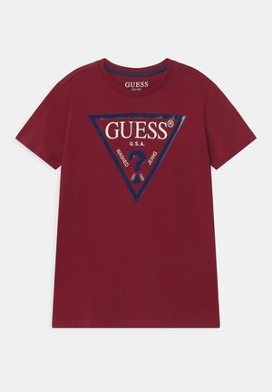 Rood T-shirt met korte mouwen met groot GUESS-driehoeklogo omrand in marineblauw en vraagteken op de borst gedrukt. Geen mensen aanwezig.