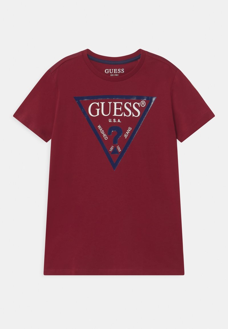 T-shirt rouge à manches courtes avec un grand logo triangle GUESS bordé de bleu marine et un point d'interrogation imprimés sur la poitrine. Aucune personne présente.