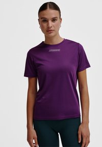 Lila aktiv t-shirt med korta ärmar, rund halsringning, slät textur och en kontrasterande vit "HUMMEL"-logotyp över bröstet.
