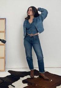 Denim jack en crop top set in middelblauw, gecombineerd met hoge taille blauwe jeans en bruin slangenprint enkellaarsjes op een patroon vloerkleed.