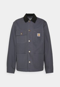 Giacca grigia scura con colletto in velluto a coste nero, bottoni in metallo, due tasche frontali e un patch con logo sul petto. Design strutturato e tessuto resistente.