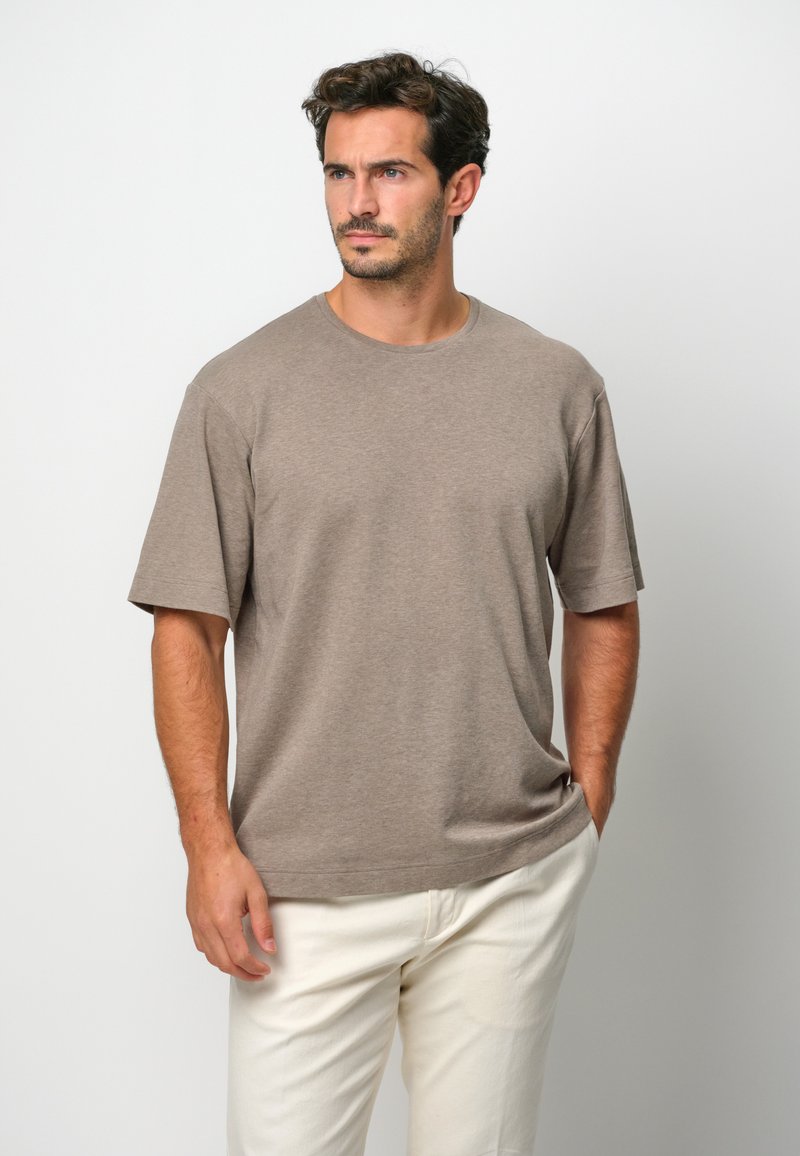 T-shirt z krótkim rękawem i okrągłym dekoltem w jasnobrązowym kolorze wykonany z bawełny, o luźnym kroju i gładkiej fakturze, zestawiony z białymi chinosami.