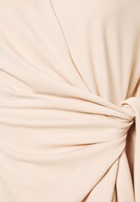 Sezione con vestito avvolgente nudo, realizzato in tessuto arricciato, con una texture morbida e una finitura liscia, fissato con un dettaglio annodato sul lato.