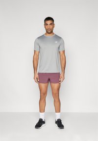 T-shirt de sport gris à manches courtes, avec un logo subtil. Associé à un short bordeaux et des baskets noires, le tout complété par des chaussettes blanches.