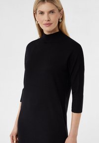 Schwarzes Strickkleid mit hohem Kragen, drei Viertel langen Ärmeln und gerippten Texturdetails an den Ärmeln. Glatte Oberfläche.