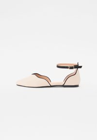 Pantof cu balet plat în bej deschis, cu vârf ascuțit, având un design cu tăieturi curbate și o curea neagră la gleznă. Textură netedă și stil minimalist.