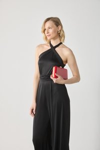 Une combinaison noire avec un design à col halter et une taille cintrée. Le modèle tient une pochette rouge brillante avec des accents dorés et plusieurs sections de couleurs.
