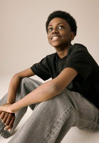 Black short-sleeve t-shirt paired with light grey, loose-fitting denim jeans. Smooth texture, relaxed design. Natural, short curly hair.