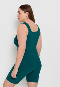 Body teal a costine con scollatura quadrata e spalline larghe, abbinato a pantaloni corto coordinati. Texture liscia e forma aderente.