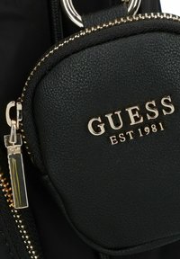 Borsa a tracolla in pelle nera con dettagli in metallo dorato. Presenta una zip e il logo del marchio in rilievo "GUESS EST 1981". Texture liscia.