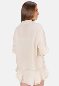 White, textured cotton short-sleeve shirt with fold-over collar and rolled sleeves, worn over a matching ruffled skirt.
