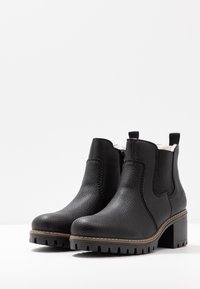 Bottines noires avec une finition en cuir texturé, des tirettes, des zips sur les côtés et une semelle épaisse rainurée. Accents cousus sur les bords.