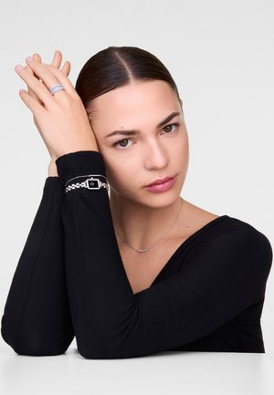 Bijoux en argent comprenant un bracelet avec un cadran noir rectangulaire, un collier en argent délicat et un haut texturé noir.
