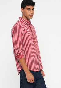 Rød og hvitstripet skjorte med knapper, lange ermer, smale striper og krage. Stoffet ser glatt ut med en avslappet passform.