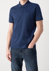 Námořnická polokošile vyrobená z měkké bavlny, s dvoupoložkovým knoflíkovým zapínáním a krátkými rukávy. Malá výšivka loga na hrudi. Nosená s tmavými džíny.