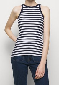 Marinblus med vita ränder, ärmlös med ribbat mönster, rund halsringning och kontrasterande kant. Tillsammans med mörkblå denimjeans.