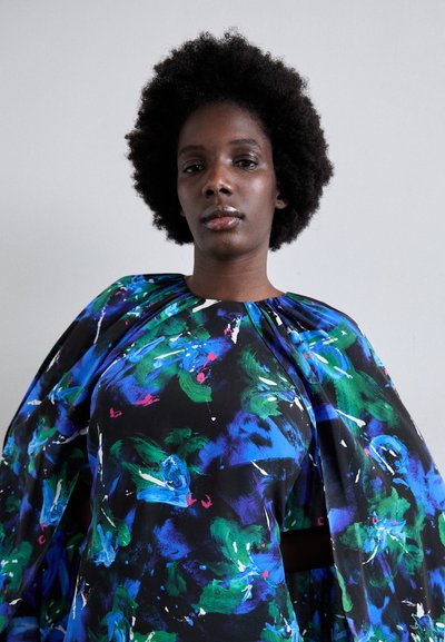 Blouse colorée au design fluide, base noire ornée de motifs abstraits vibrants en bleu, vert et rose, se terminant par un col froncé.